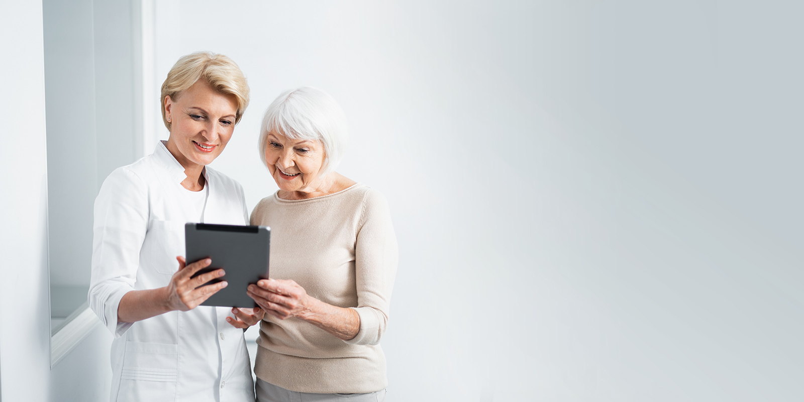 Zahnärztin erklärt älterer Patientin etwas an einem Tablet
