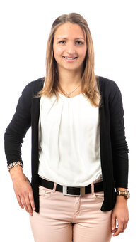 Stehende Person blickt frontal in die Kamera, Hände locker seitlich. Trägt weiße Bluse, schwarzen Cardigan, hellrosa Hose mit schwarzem Gürtel und Armbanduhr. Vor weißem, nahtlosem Hintergrund.