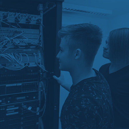 Serverrack mit Patchpanel und Netzwerkgeräten – zwei Personen prüfen Verkabelung und Bedienelemente – Kontext: Technikraum mit offenem Rack, sichtbaren Ethernetkabeln, Schaltern und Leuchten, monochrome blaue Farbgebung.