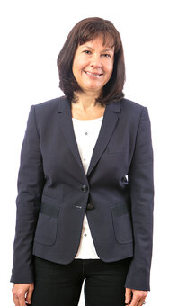 Margarete Hammerl, Erwachsene Person mit mittellangem braunem Haar in dunkelblauem Blazer und weißem Oberteil steht frontal, Arme locker herabhängend, vor weißem Studiohintergrund; Oberkörper bis Hüfte sichtbar, schwarze Hose.