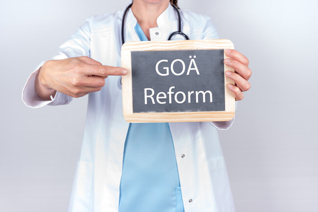 Ärztin im weißen Kittel hält eine Tafel mit der Aufschrift "GOÄ Reform" in den Händen