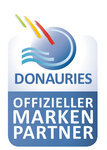 Rechteckiges Logo-Abzeichen zeigt blauen Kreis mit drei farbigen Streifen und blauen Wellen; unten blaues Textfeld in Versalien. Vollständiger Text: DONAURIES OFFIZIELLER MARKEN PARTNER.
