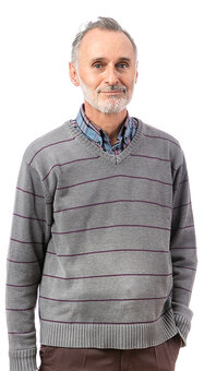 Älterer Mann mit grauem Haar und kurzem Bart steht frontal, eine Hand in der Hosentasche, Blick zur Kamera, trägt grauen gestreiften V-Pullover über kariertem Hemd, isolierter weißer Hintergrund.